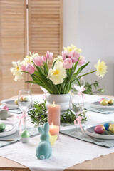 Festive Easter table setting with vase of flowers, cutlery, candles and painted eggs