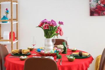 Festive Easter table setting with vase of flowers, cutlery, glasses and painted eggs