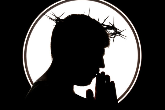 Silhouette of man in Jesus robe and crown of thorns praying on black background