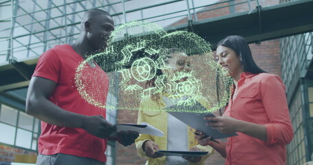 Image of cloud with cog wheels over diverse colleagues discussing work in office