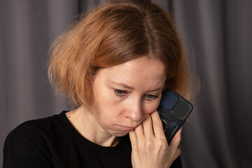 Sad woman with smartphone at home, sitting indoors with serious expression, experiencing loneliness...