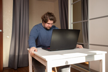 Angry man working on laptop, resentment during online project, stress in casual study room.