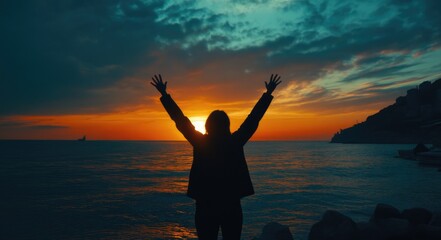 Fototapeta premium Silhouette of a woman with raised arms against a sunset sky over a sea background.