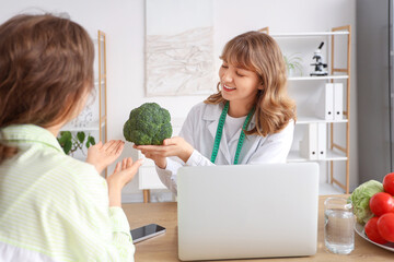 Female nutritionist showing broccoli to patient at table in office