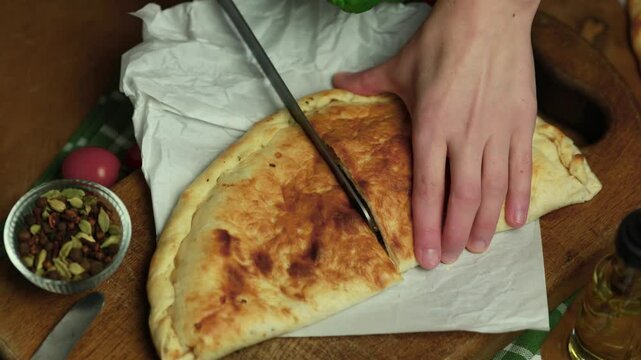 woman cuts in half calzone with salami, ham, cheese, tomato, basil, mushrooms, cream sauce on a wooden background, Italian pastries, traditional Italian cuisine, olive oil with spices, food photo