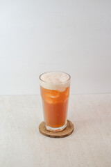 Refreshing Chilled Lychee Tea Served In A Tall Glass With Ice Cubes And Light Foam On Top, Placed On A Wooden Coaster Against A Light Background.