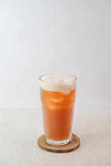 Refreshing Iced Lychee Tea In A Tall Glass With Foam Layer And Ice Cubes On A Wooden Coaster Against A Light Background.