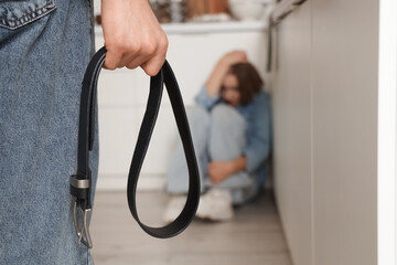 Man with belt hurting his wife in kitchen, closeup. Domestic violence concept