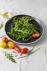 Vegetarian fresh arugula salad with cherry tomatoes, olive oil and spices on plate. Salad ingredients.