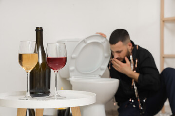 Glasses of wine on table against man feeling unwell after party in restroom, closeup