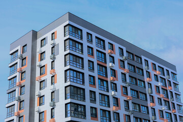 Fototapeta premium The concept of modern architecture, a residential complex, an apartment building for living. Close-up view from the corner of a multi-storey, apartment building in gray and white tones with orange
