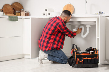 Male plumber repairing sink pipe in kitchen