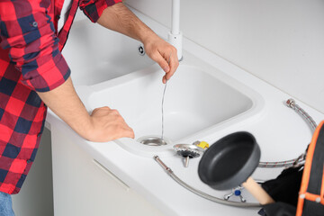 Male plumber with wire clearing drain in kitchen, closeup © Pixel-Shot