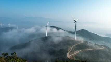 Wind turbines on a foggy mountain range. © Wirestock