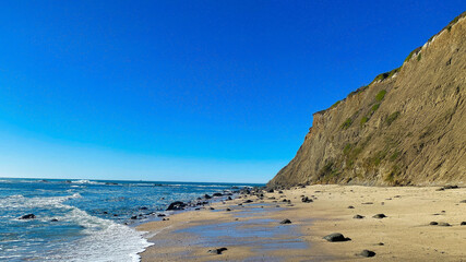 A cliff is by a beach with waves on the ocean. The blue sky has copy space in this beautiful background. 