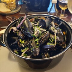 Steamed mussels in a black pot, garnished with herbs and red onion, served at a restaurant table. Food photography. Ideal for food, seafood, or restaurant themes.