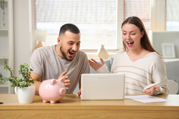 Happy young couple with laptop at table in room. Refund concept