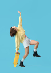 Young woman with skateboard dancing on blue background