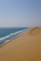 Towering sand dunes cascade towards the ocean, shaping an otherworldly landscape in Sandwich Harbour. The meeting point of the desert and sea creates a mesmerizing, untouched natural beauty.