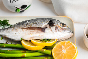 Fresh raw Dorado with asparagus spices, herbs, lemon and salt over white background.