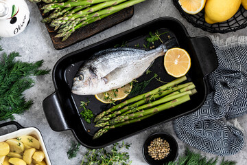 the concept of a delicious dinner. raw dorado fish with asparagus and lemon on dark background.