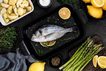 the concept of a delicious dinner. raw dorado fish with asparagus and lemon on dark background.