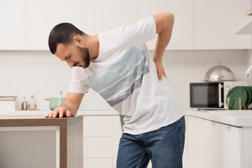 Young man suffering from back pain in kitchen
