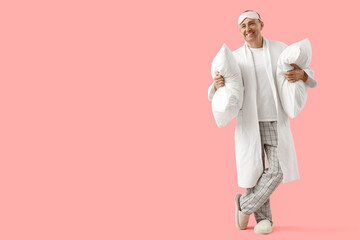 Mature man with sleeping mask and pillows on pink background