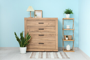 Wooden commode and stand with plants near blue wall in room