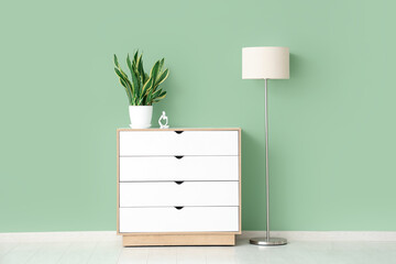 Plant with statuette on commode and lamp near green wall in room
