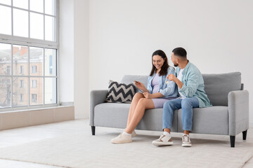 Young pregnant couple with house rental agreement and key sitting on sofa in room