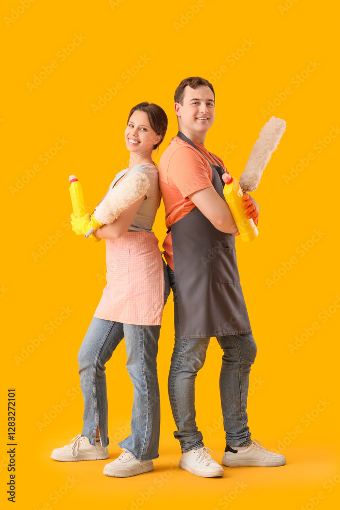 Poster Young couple with cleaning supplies on color background