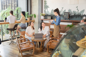 Young waitress barista worker takes bakery orders from group customers females in cafe restaurant, Asian single businesswoman open coffee bakery shop, small business entrepreneur start-up lifestyle
