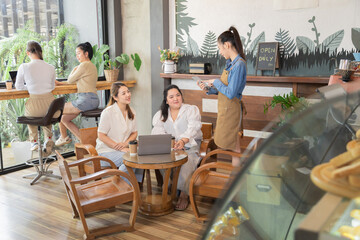 Young waitress barista worker takes bakery orders from group customers females in cafe restaurant, Asian single businesswoman open coffee bakery shop, small business entrepreneur start-up lifestyle
