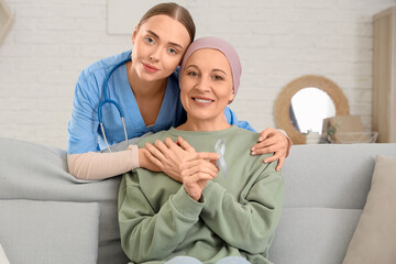 Nurse hugging mature woman after chemotherapy on sofa at home. Brain cancer concept