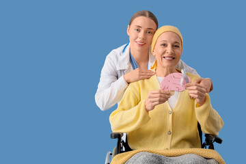 Fototapeta premium Mature woman after chemotherapy in wheelchair with grey awareness ribbon and doctor on blue background. Brain cancer concept