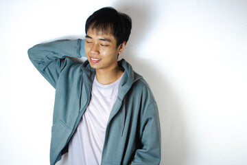 Asian teenager in white t-shirt and blue hoodie, blushing with his right hand behind his head