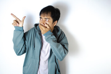 Asian teenager in white t-shirt and blue hoodie, posing with mouth closed and pointing to the right