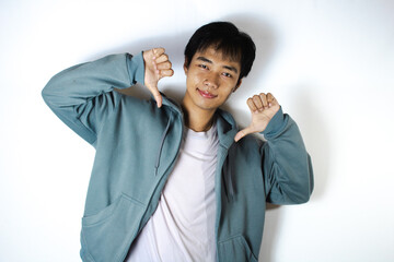 Asian teenager in white t-shirt and blue hoodie, doing "DISLIKE" pose with smile