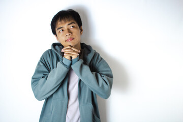 Asian teenager in white t-shirt and blue hoodie, posing hopefully with hands clasped