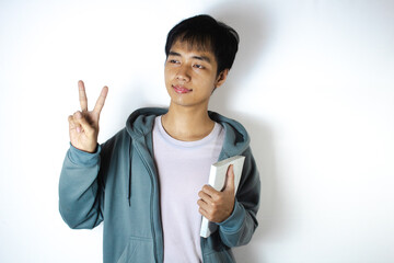 Asian teenager in white t-shirt and blue hoodie, posing with two fingers while holding a book