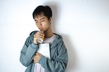 Asian teenager in a white t-shirt and blue hoodie, posing in deep thought while hold a galss of can