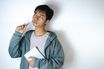 Asian teenager in white t-shirt and blue hoodie, posing daydreaming with a pen on his cheek