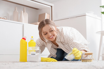 Young woman with baking soda cleaning carpet in kitchen