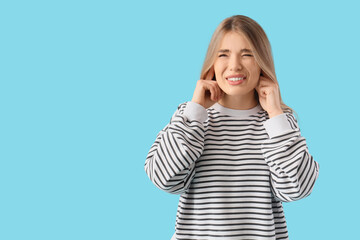 Young woman suffering from loud noise on blue background