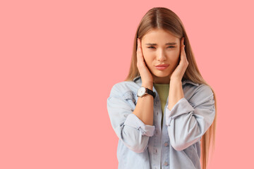 Young woman suffering from loud noise on pink background