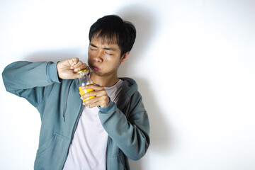 Asian teenager in white t-shirt and blue hoodie, posing with drink in mouth and cap on bottle
