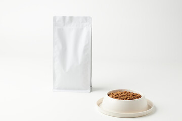 Dry Pet Food Packaging Next to Food Bowl Filled With Kibble on a Plain Background