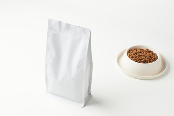 White Packet of Pet Food Beside a Small Bowl Filled With Dry Food on a Light Surface
