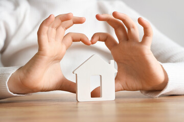 Cute girl with house figure making heart gesture at table, closeup. Adoption concept